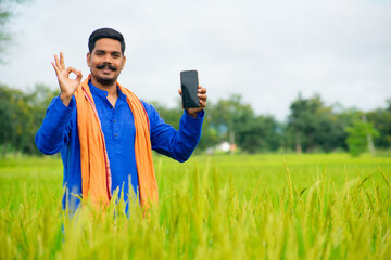 Young Indian farmer Showing a mobile screen at green agriculture field