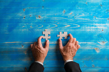 Top View Of Hands Of A Businessman Holding Two Blank Matching Puzzle Pieces
