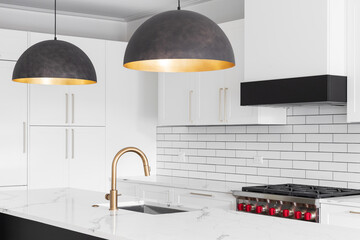 A kitchen sink detail shot with a gold faucet, white cabinets, marble countertop, and subway tile backsplash.