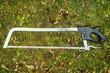 Top view of a metal meat saw with a black handle on the grass
