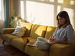 © ZHPH Production/Stocksy - Woman with laptop and notebook sitting on the sofa at home