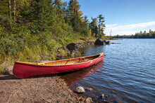 Red Wooden Canoe On A Northern Minnesota Lake With Rocks And Pines Along The Shore