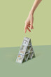 © Yaroslav Danylchenko/Stocksy - Dollars in pyramid shape with hand reaching out.