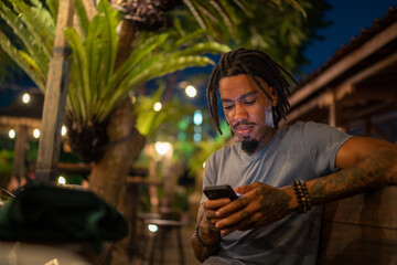 Tattooed black man using smartphone sitting at restaurant