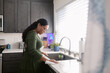 © ByLorena/Stocksy - Mixed race woman wearing glasses cleaning the kitchen