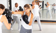 Young concentrated woman practicing boxing punches in sparring during group self defence course in gym