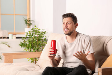 Wall Mural - Disappointed man with can of beverage on sofa indoors