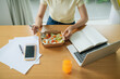 © Marc Tran/Stocksy - Businesswoman eating fresh salad near coffee to go and laptop