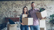 © silverkblack - Portrait of happy young couple standing in bedroom in new house, holding carton boxes, smiling and looking at camera. Family, relationship and relocation concept.
