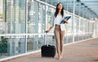 © Anela R/peopleimages.com - Airport, corporate manager and travel for company business seminar or convention workshop. Happy businesswoman walking with suitcase bag, files in hand and smiling in urban city outdoors