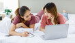 © Bangkok Click Studio - Millennial Asian young happy cheerful female teenager LGBTQ lesbian lover couple laying down together on bed and pillow learning studying online via laptop computer and writing short note on notebook