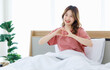 © Bangkok Click Studio - Millennial Asian young happy cheerful female teenager sitting laying smiling on pillow under thick warm blanket on cozy bed in bedroom at home in morning
