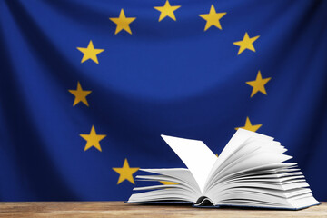 Wall Mural - Open book on wooden table against flag of European Union. Space for text