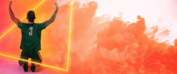 Wall Mural - Rear view of caucasian player with arms raised kneeling over illuminated triangle and orange smoke