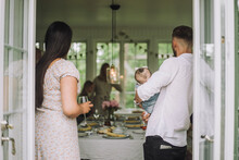 Woman With Wineglass Standing By Man Carrying Daughter At Party Seen Through Doorway