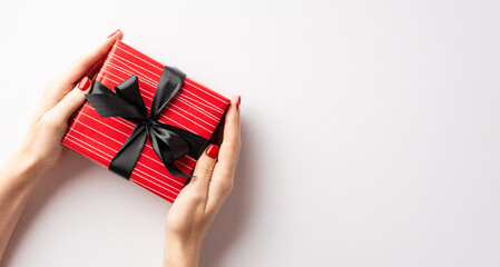 Wall Mural - Black friday shopping concept. First person top view photo of young woman's hands giving red giftbox with black bow on isolated white background with copyspace