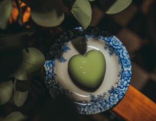 Vertical closeup of green sweet in the heart form in the white plate with blue decoration