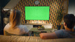 © Framestock - Couple sitting on sofa in living room, talking, watching breaking news, movie or series on TV. Wife and husband resting and chilling at home in the evening together. Green screen. Chromakey.