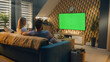 © Framestock - Couple sitting on sofa in living room, talking, watching breaking news, movie or series on TV. Wife and husband resting and chilling at home in the evening together. Green screen. Chromakey.