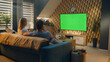 © Framestock - Couple sitting on sofa in living room, talking, watching breaking news, movie or series on TV. Wife and husband resting and chilling at home in the evening together. Green screen. Chromakey.