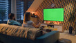 © Framestock - Woman switching channels with remote control. Couple sitting on couch in living room, talking, watching breaking news, movie or series on TV. Resting at home in the evening. Green screen. Chromakey.