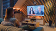 © Framestock - Couple sitting on sofa in living room with snacks, watching politics TV news about European Union and new sanctions package against Russia. Spending evening together at home. TV live broadcasting.