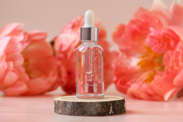 Frozen glass dropper bottle with silver cap on woooden podium with peonies in soft focus as background. Pipette with fluid hyaluronic acid, serum, retinol. Natural cosmetics, healthcare, beauty mockup