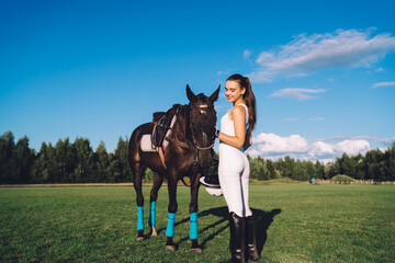 Happy young horsewoman caressing horse on green lawn