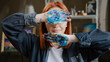 © Yuliia - Red-haired Caucasian woman lady girl painter student of art school looking at camera indoors workshop drawing painting holding showing hide behind dirty hands palms close face eyes with arms in paints