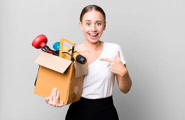 caucasian pretty woman looking excited and surprised pointing to the side with a tool box. repair home concept