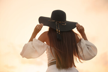 Young woman in hat at sunset, back view