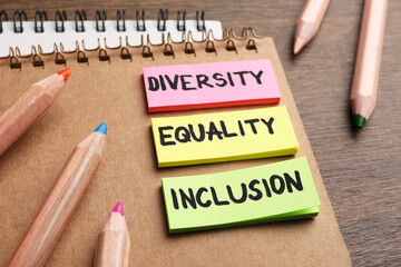 Wall Mural - Sticky notes with words Diversity, Equality, Inclusion, notebooks and colorful pencils on wooden table, closeup