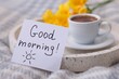 Cup of coffee, flowers and card with phrase GOOD MORNING! on knitted paid, closeup