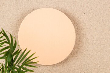 Blank empty beige round platform podium for cosmetics or products presentation on white beach sand background. Top view to blank circle podium and green palm leaves on natural sand