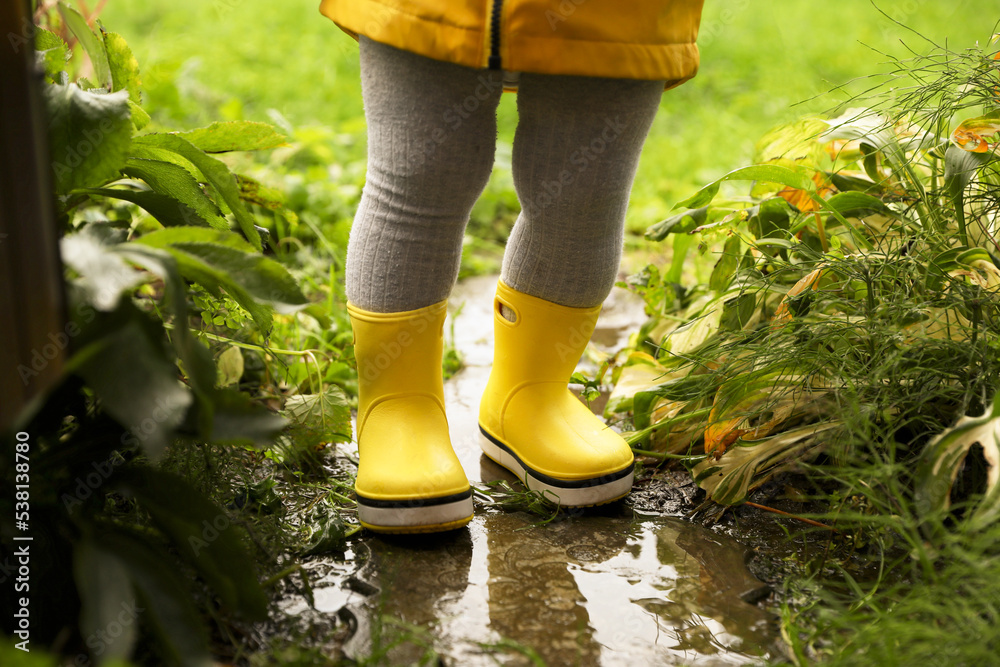 Little girl wearing rubber boots standing in puddle outdoors, closeup ...