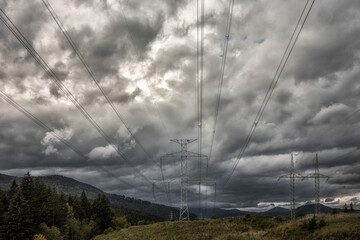 Wall Mural - High voltage towers with electricity transmission power lines in country under dark clouds