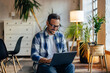 © bnenin - Smiling businessman working at the co-working space, sitting with a laptop on his lap.