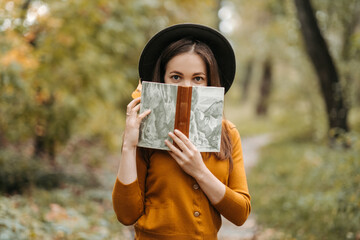 Portrait of a woman in a hat. A young candid woman in a knitted sweater and a brown hat is walking in the park and reading a book. French girl. Student preparing for exams