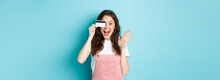 Excited And Surprised Young Woman Holding Plastic Credit Card Over Eye, Scream Of Joy While Shopping, See Something Cool To Buy, Standing Over Blue Background