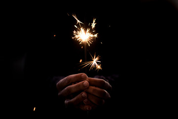 Human people hands holding fire sparkler in black background. Concept of holiday and fun. Hope and future with copy space. Close up. Party event and loneliness. One woman celebrate alone in the dark