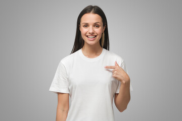 Wall Mural - Young woman pointing with index finger at blank t-shirt with empty space for your advertising text