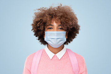 Wall Mural - Portrait of smiling african american school girl or college student with curly wearing medical mask