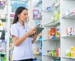 © CandyRetriever  - Medical pharmacy and healthcare providers concept. Attractive Asian woman pharmacist working on digital tablet checking stock of medical product, drugs, medicine and supplements on shelf in drugstore.
