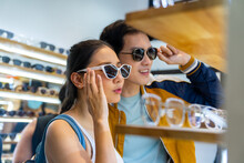 Young Asian Couple Enjoy And Fun Outdoor Lifestyle Shopping Together At Street Market On Summer Holiday Vacation. Happy Man And Woman Choosing And Buying Fashion Sunglasses Together At Street Market.