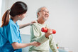 © Kiattisak - Asian Senior old man doing physiotherapist with support from caregiver. Mature male sitting on sofa in living room using dumbbell workout exercise. Healthcare medical concept.