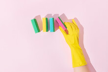 Colorful cleaning sponges and hand in yellow rubber glove trendy composition. Minimal bright pink background with sunlit shadows and copy space. Creative home cleaning concept. Flat lay. Top view.