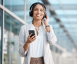 © Anela Ramba/peopleimages.com - Woman, smartphone and headphones listening to music, radio or podcast on break in cityscape. Young professional, business person and streaming online service, audiobook and subscription playlist.