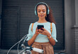 © Kay Abrahams/peopleimages.com - Music, bicycle and girl on her phone in the city with headphones on. Technology, summer fashion and young woman on her smartphone streaming song, track and radio online and cycling bike in urban town