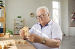 © Studio Romantic - Senior male nursing home patient trains fine motor skills for dementia or Alzheimer's disease by assembling wooden puzzles. Gray-haired mature man is sitting at table and composing brain teaser.