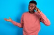 © Roquillo - young handsome man wearing pink sweater over blue background confused and annoyed with open palm showing copy space and pointing finger to forehead. Think about it.